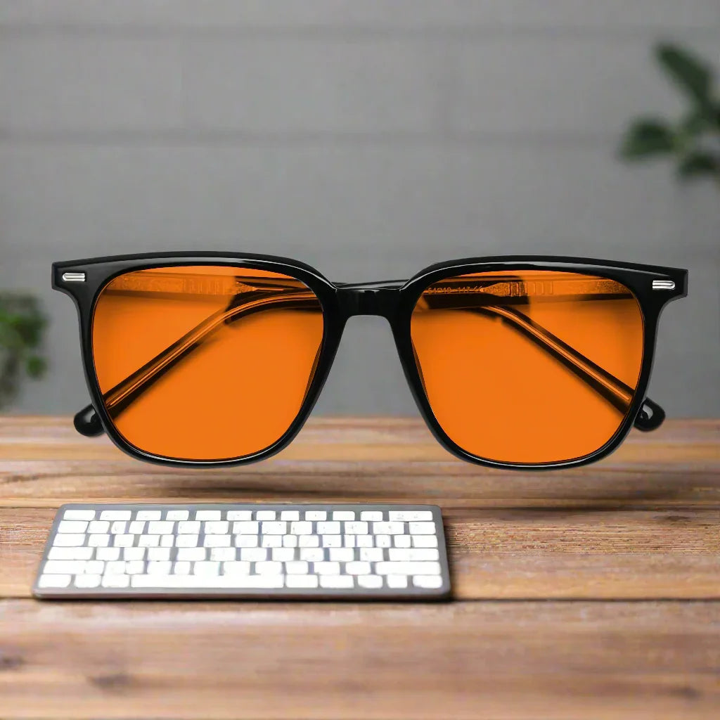 Orange lensed blue-light blocking glasses with black frame on wooden desk near white keyboard