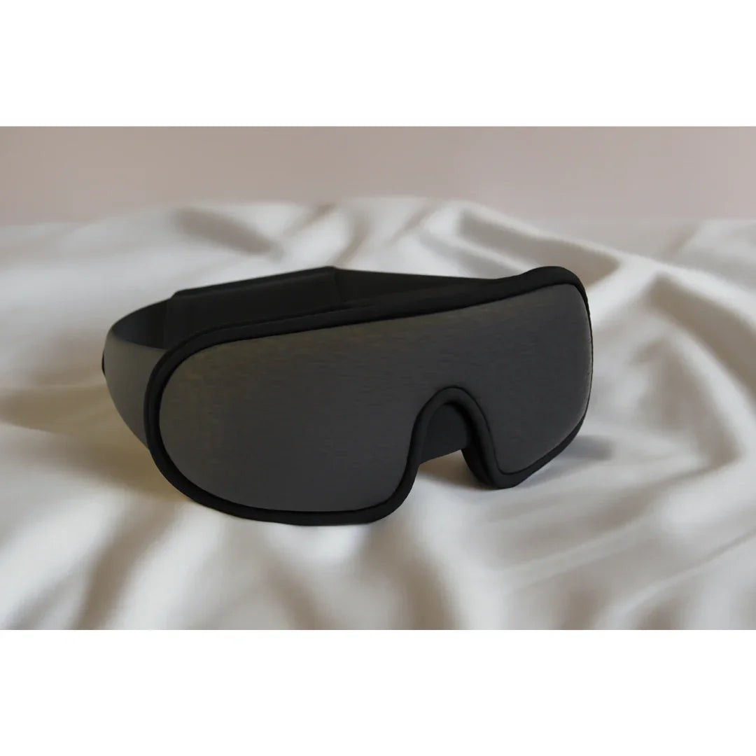 Black sleep mask with contoured eye design resting on soft white fabric