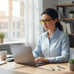 Woman wearing yellow blue light blocking glasses using laptop in bright home office