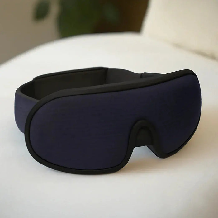 Navy blue blackout sleep mask with black trim on white surface, designed for improved sleep and relaxation